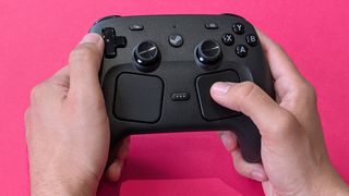 Valve Steam Controller (2026) held in two hands against a magenta card background