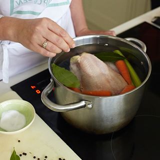 cooking chicken on black gas cooktop with carrot and water