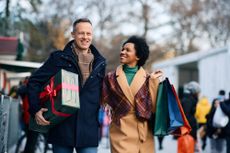 Man holds wrapped Christmas present beside woman holding bags of shopping.