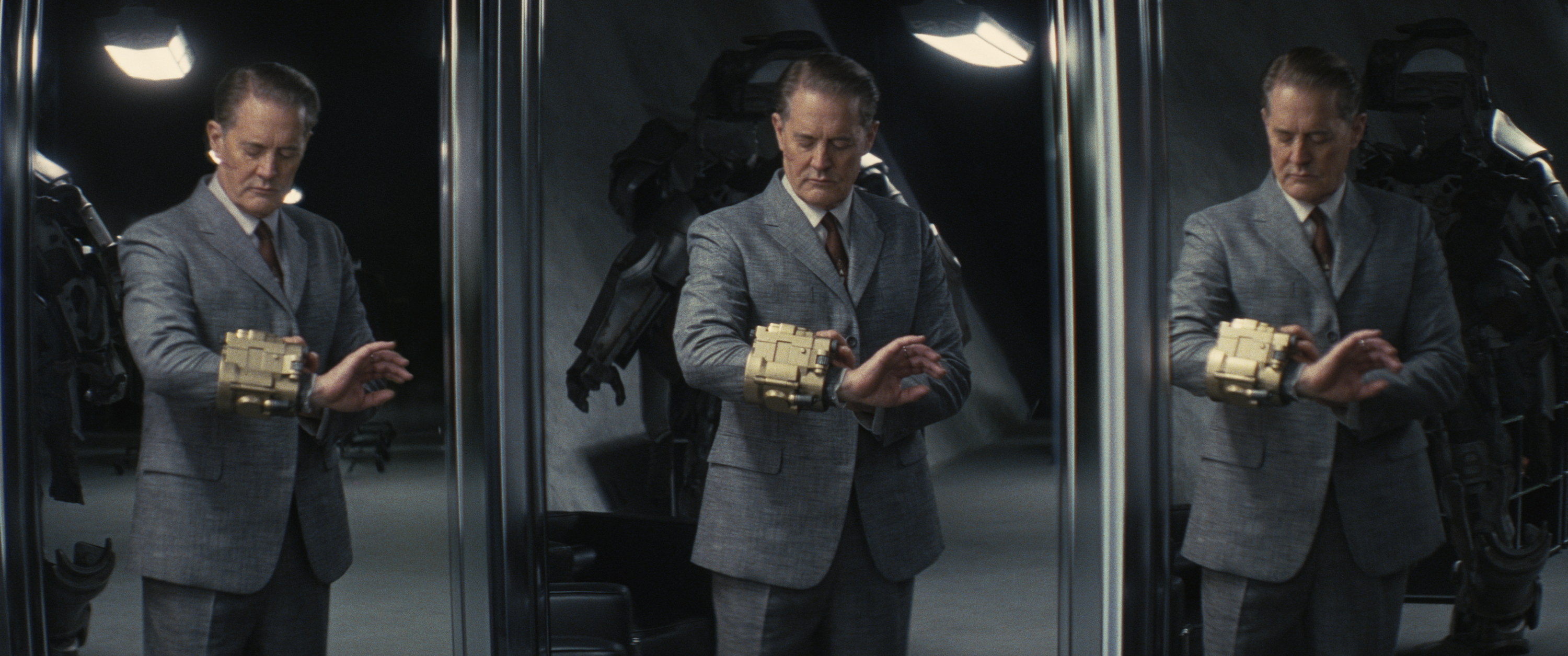 Kyle MacLachlan in a suit wearing a Pip-Boy