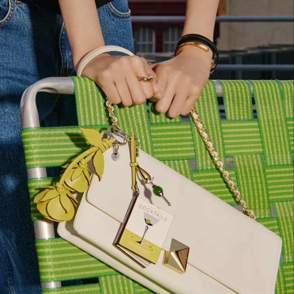 Woman holding white Kate Spade handbag on lime green deck chair.