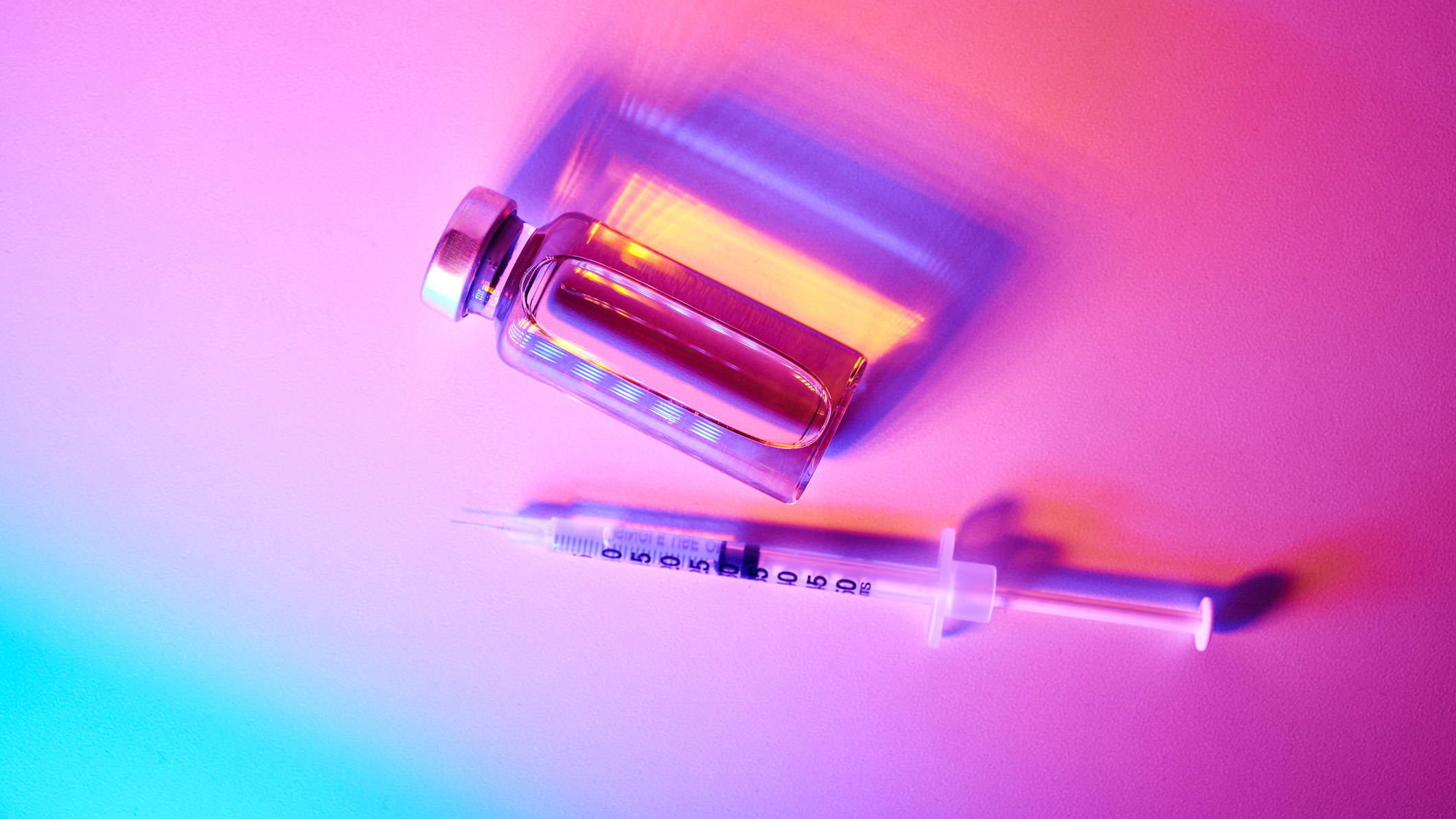 A close up of a glass bottle and syringe against a rainbow-colored background