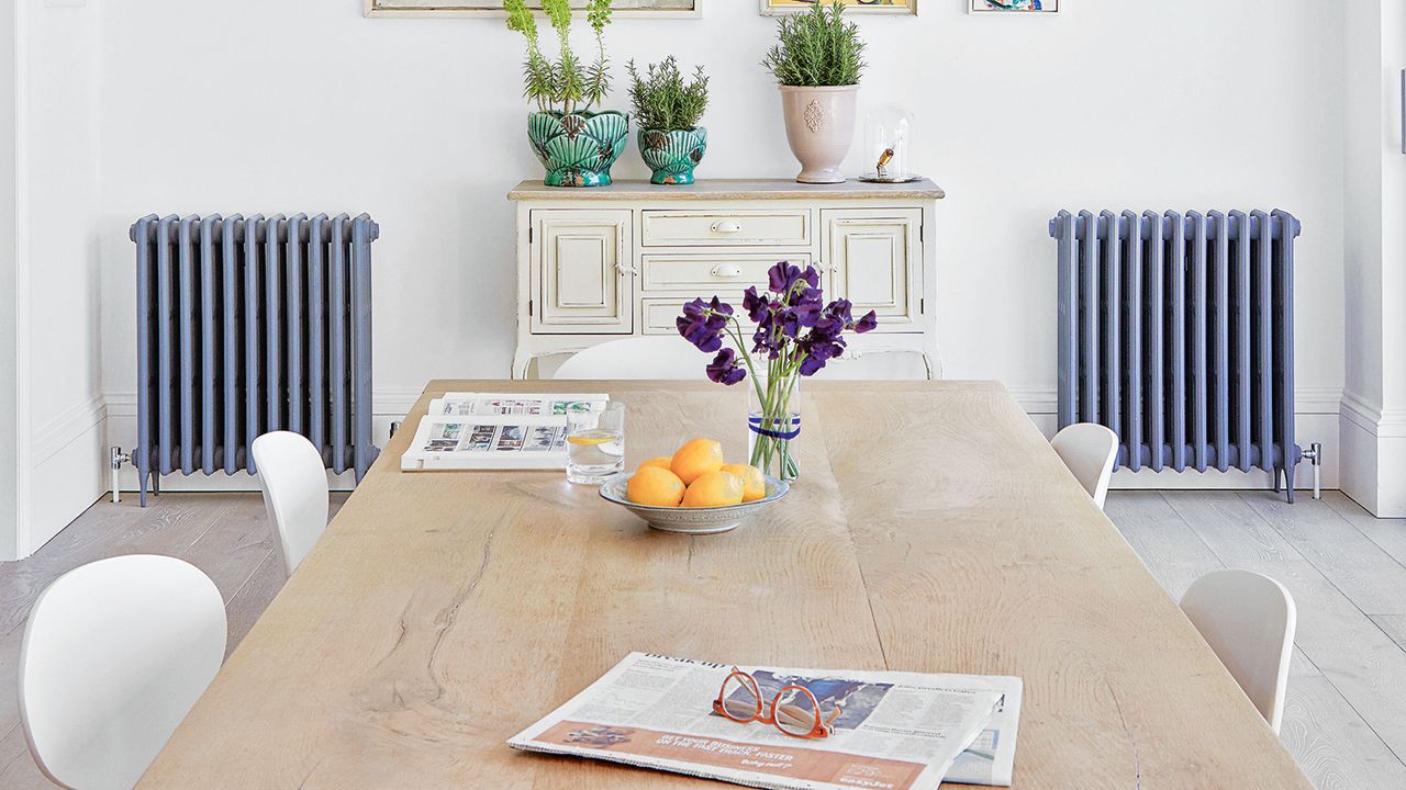 wooden dining table with white chairs in bright white dining room with gallery wall and radiators