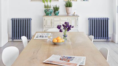 White kitchen dining room with gallery wall, pendant lights, dining table and blue cast iron radiators