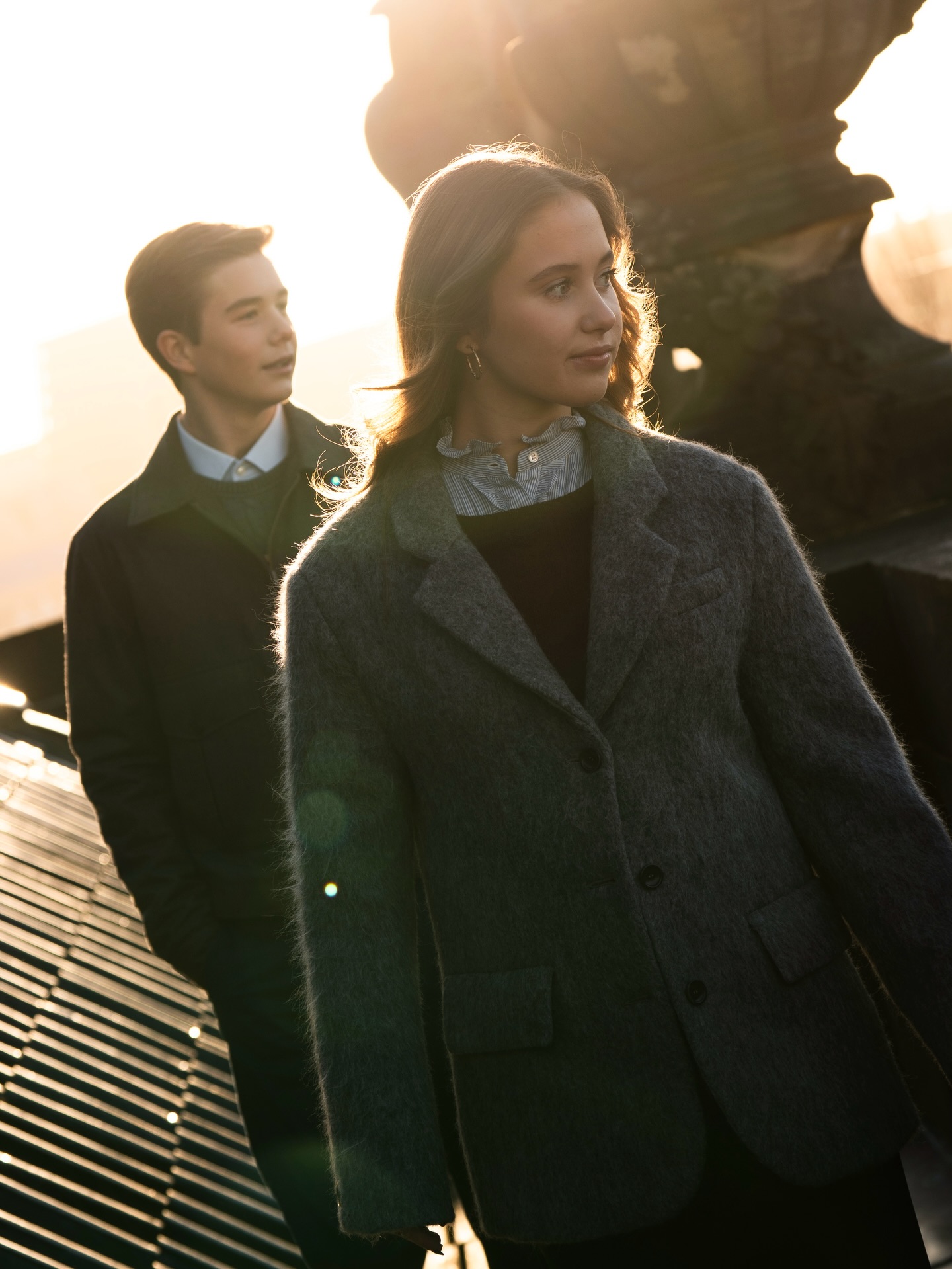 Princess Josephine wearing a gray coat with Prince Vincent walking behind her at sunset