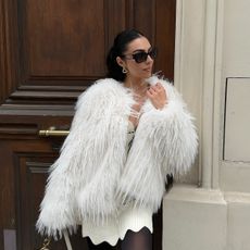 A woman wearing a white fluffy coat and sunglasses