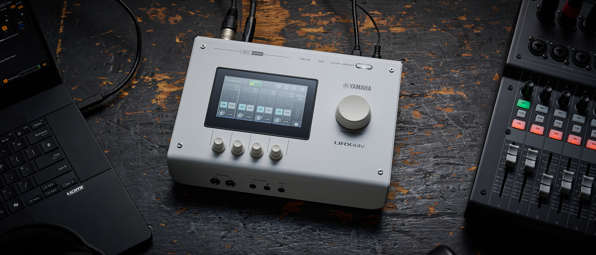 A Yamaha URX44V audio interface on a worn wooden surface with a laptop and a mixer