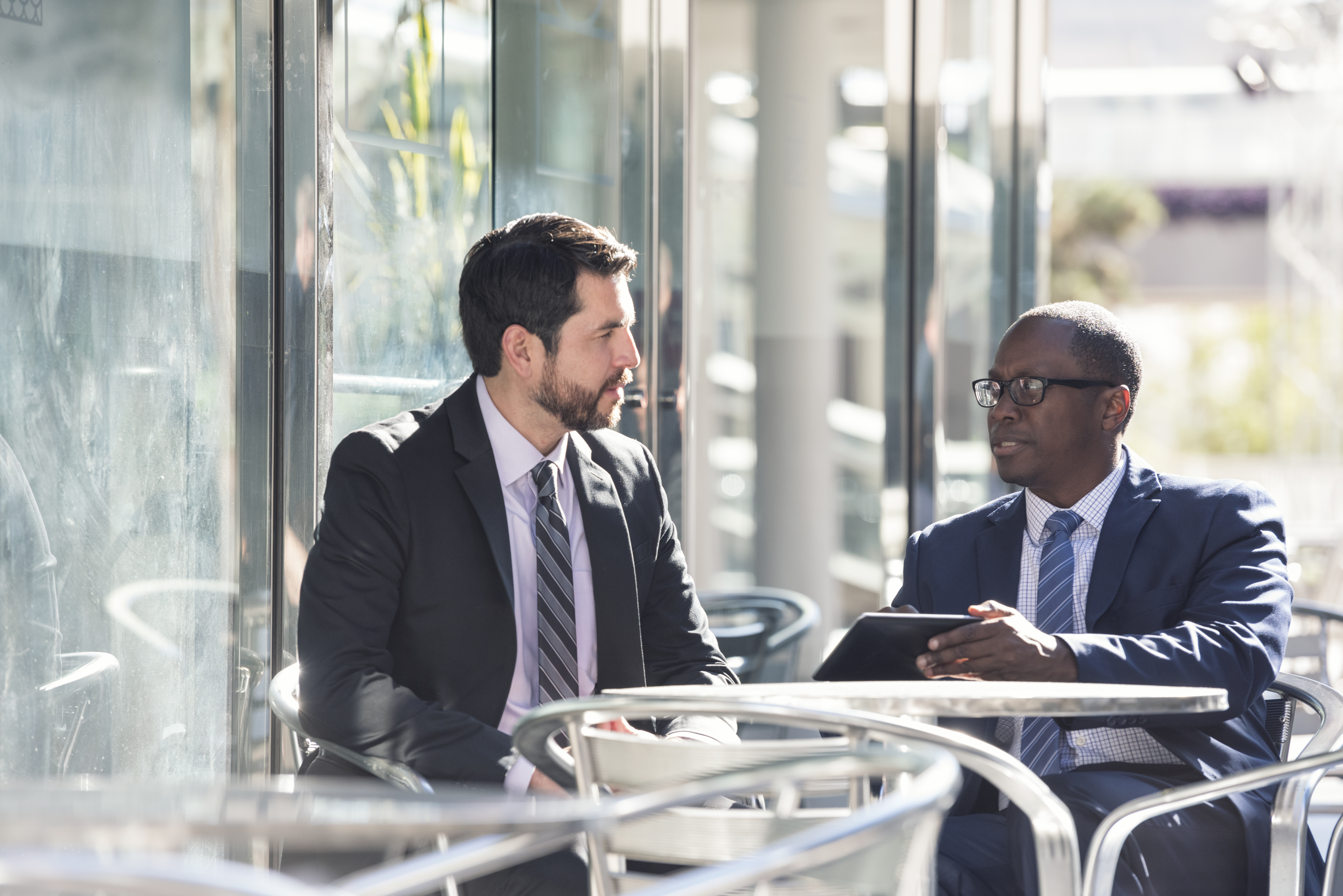 Two young businessmen sit outdoors at a restaurant.