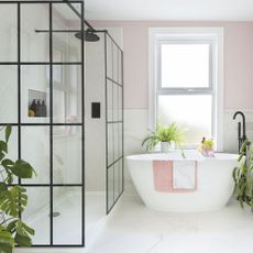Pink bathroom with white tiles on the wall and floor, and a freestanding bath next to a shower area 