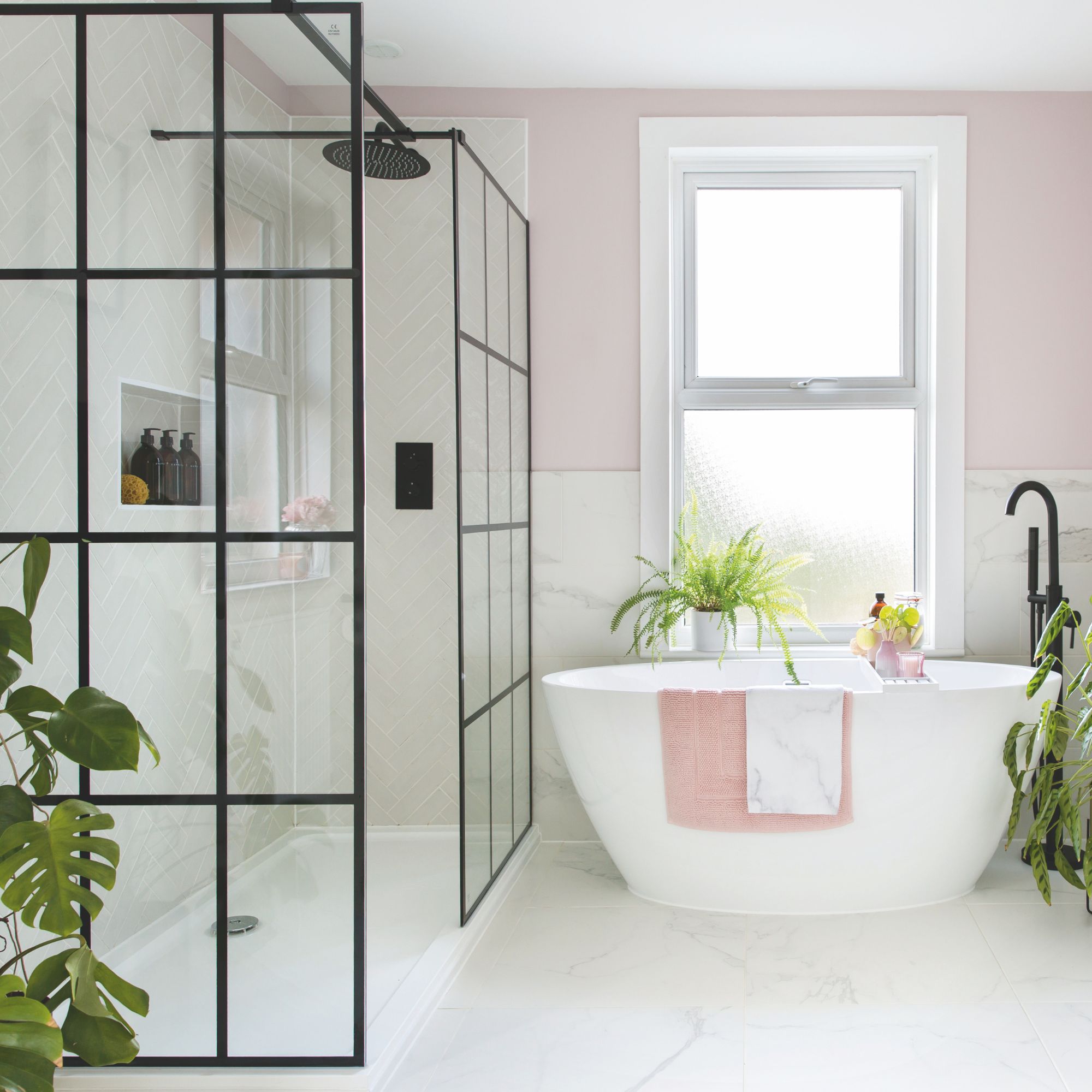 Pink bathroom with white tiles on the wall and floor, and a freestanding bath next to a shower area 