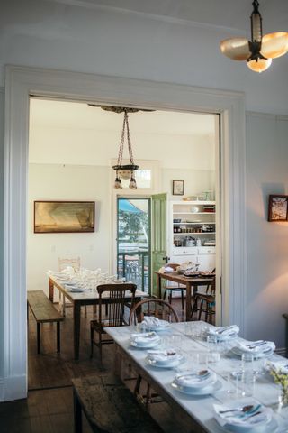 A retro-fueled dining room features wooden furniture, white tabletops, white tableware, and softly glowing pendant lights.