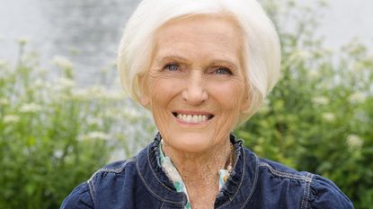 Dame Mary Berry smiles, holding a Bread and Butter Pudding.