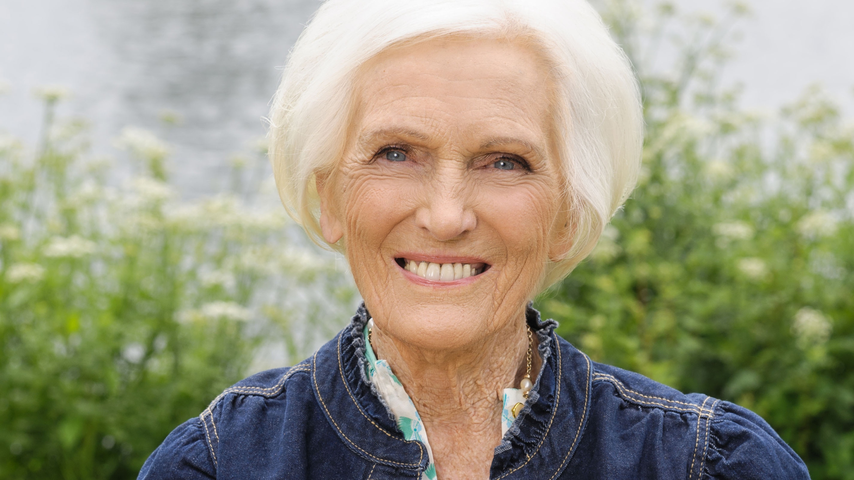 Dame Mary Berry smiles, holding a Bread and Butter Pudding.
