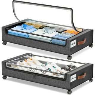 Two grey under bed storage bags on wheels with clear lids. Filled with shirts and shoes.. white background