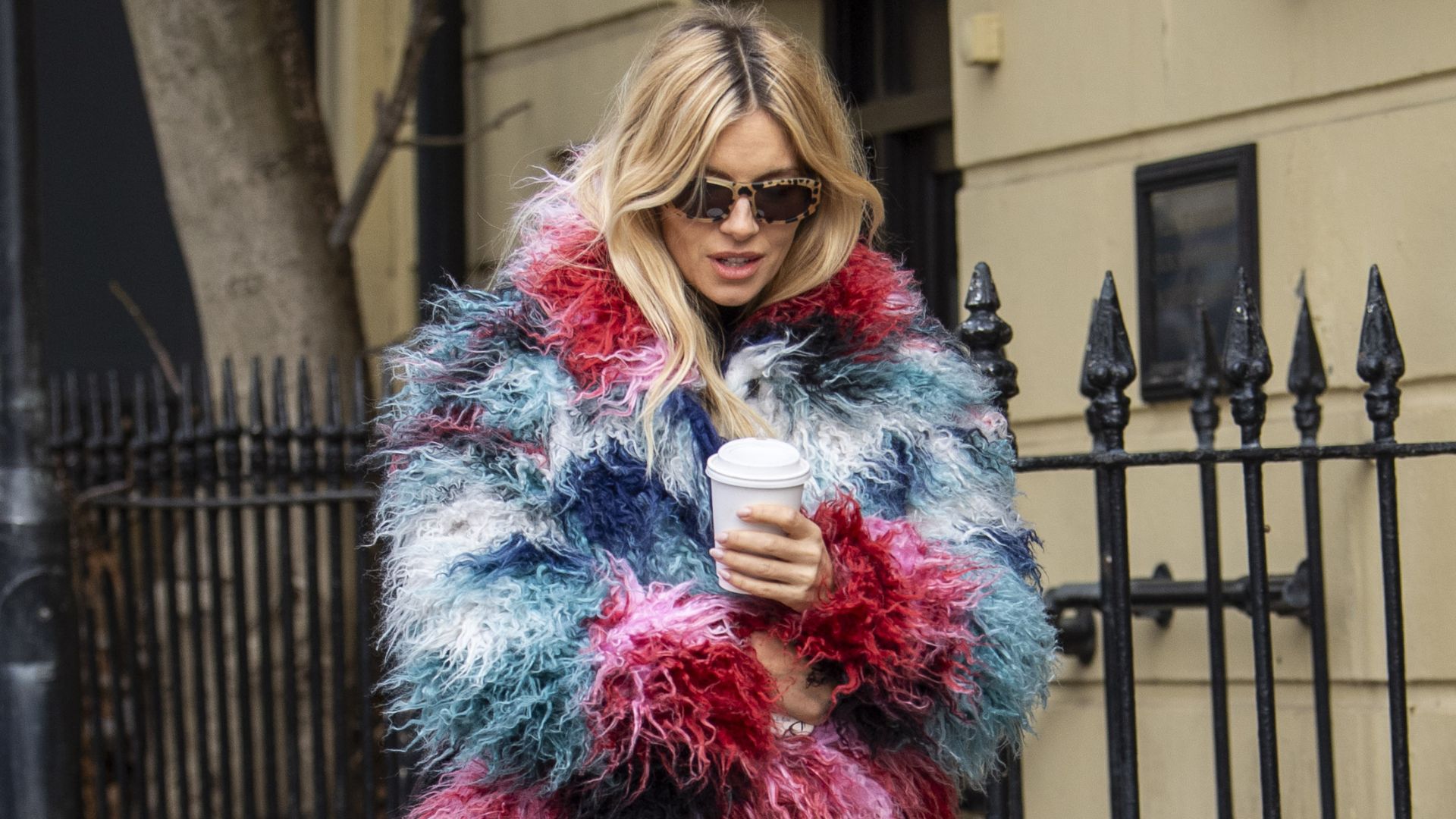 Sienna Miller walks down the street in London wearing a furry multi-coloured jacket from Desigual with white jeans and black leather ballet flats.