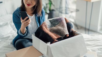 OOOOO - Cropped shot of young Asian woman doing online shopping with smartphone while unpacking parcel at home. Online hopping at home is efficient and convenience. Home Delivery service.