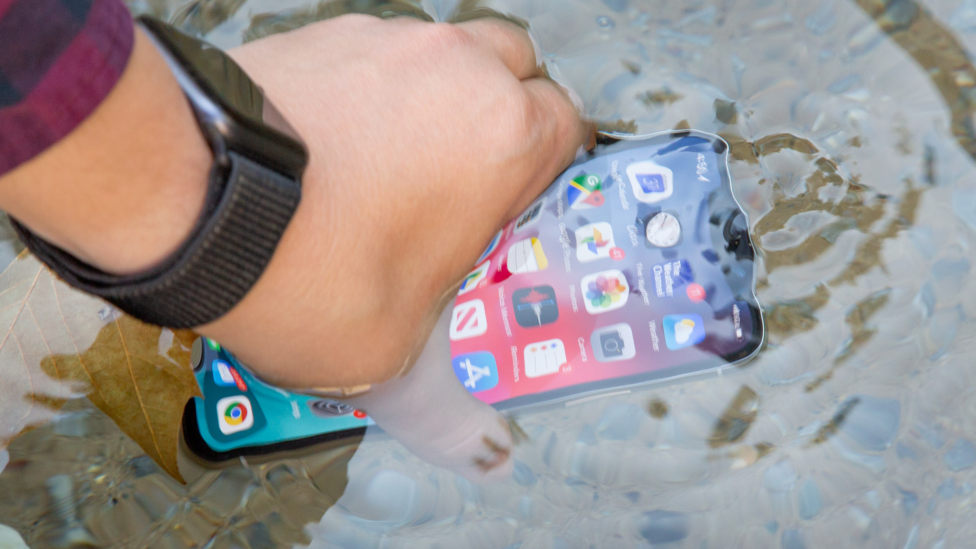 A hand dipping an iPhone in water to test its water resistance capabilities