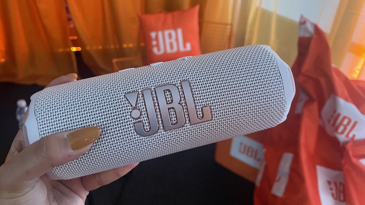 JBL Flip 7 in white finish held in hand against backdrop of orange JBL beanie bags