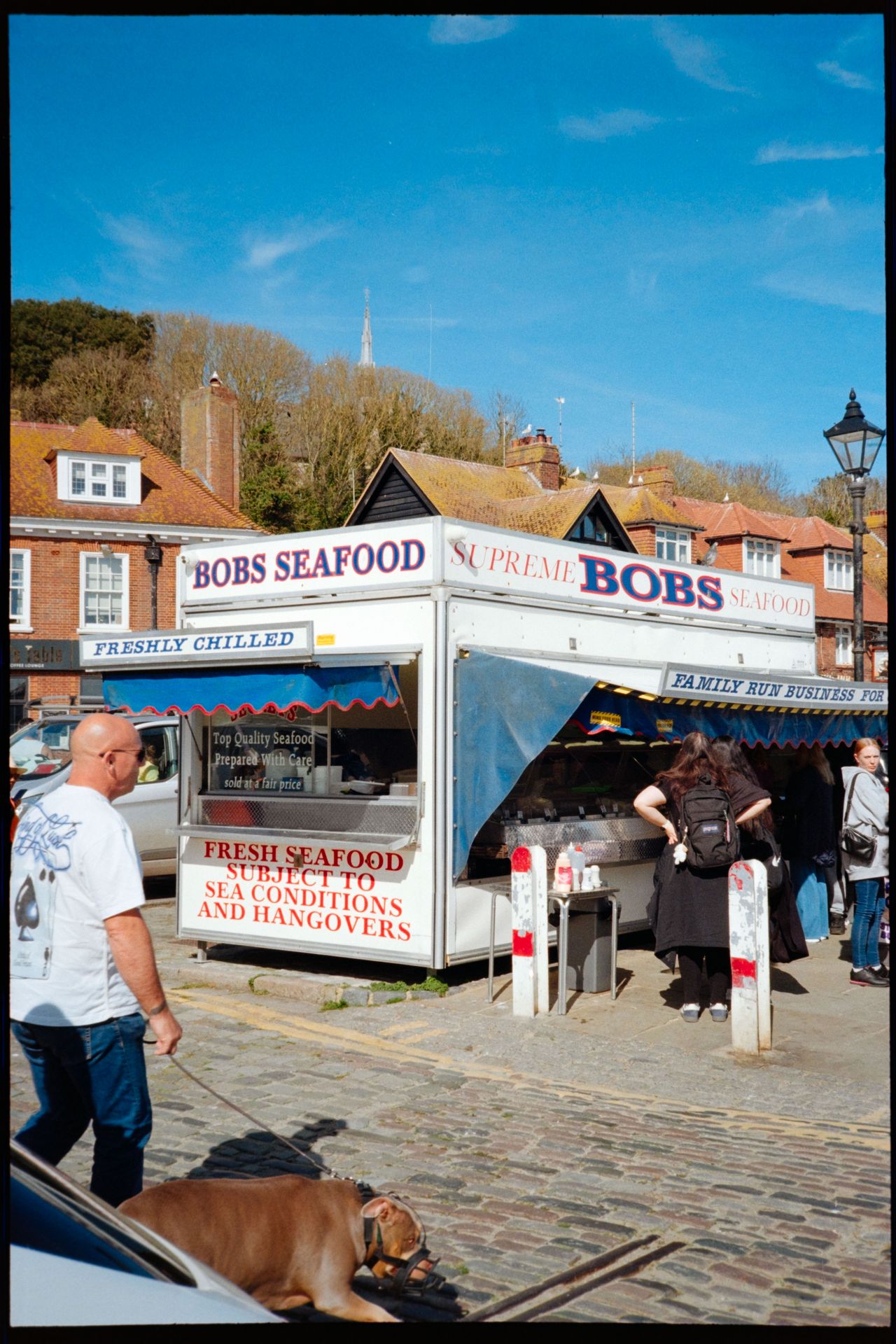 A seafood stall called Bobs Seafood on a sunny cobbled street, with people queuing outside.