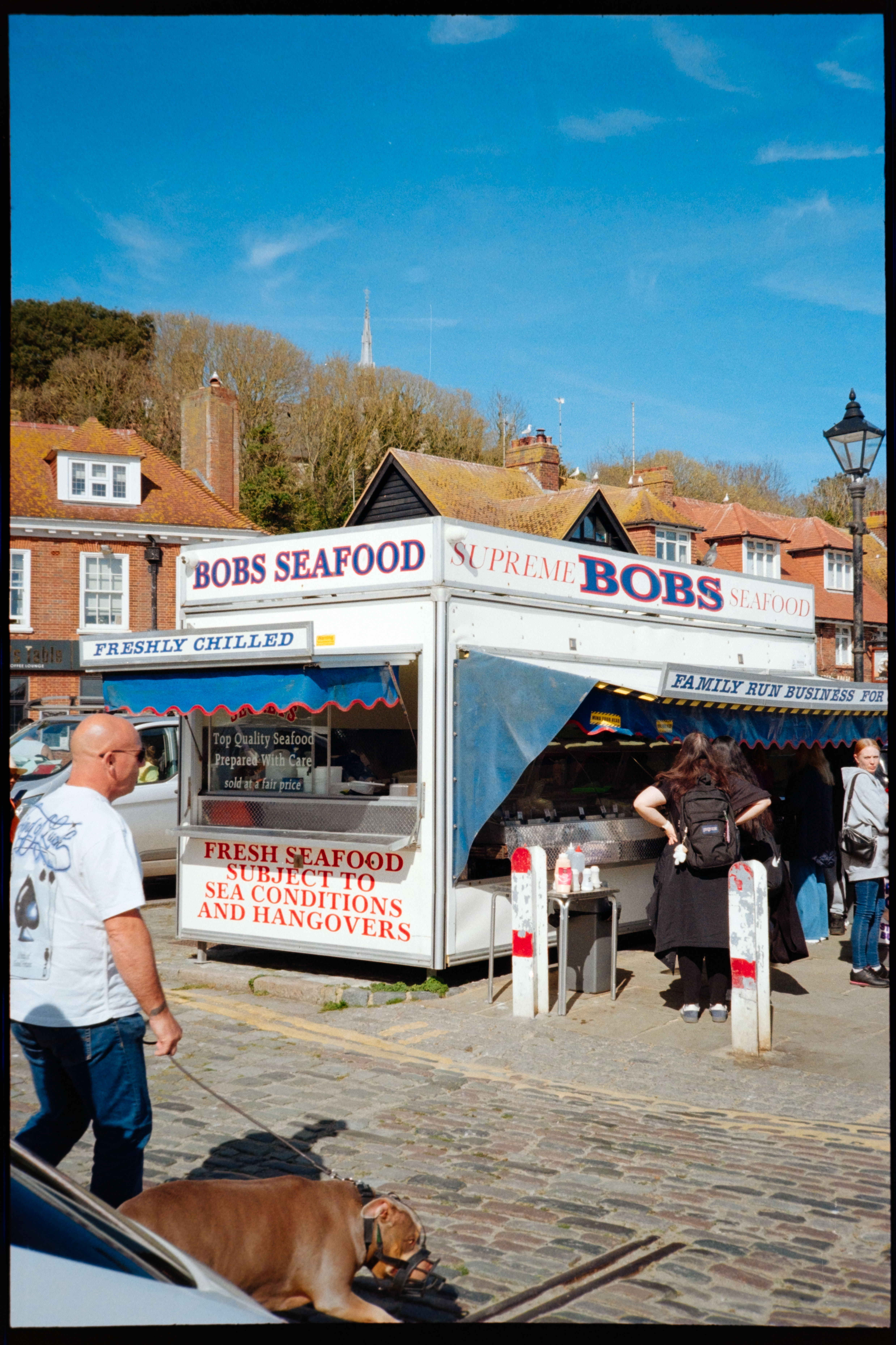 A seafood stall called Bobs Seafood on a sunny cobbled street, with people queuing outside.
