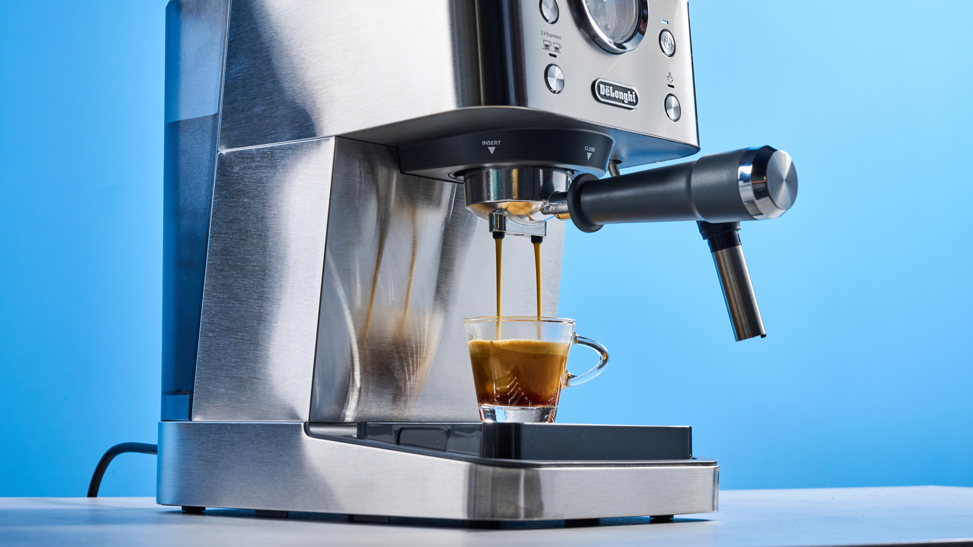 the De'Longhi Linea Classic espresso machine photographed against a blue tom's guide background, showing its silver finish, steam dial, steam wand, portafilter, and accessories