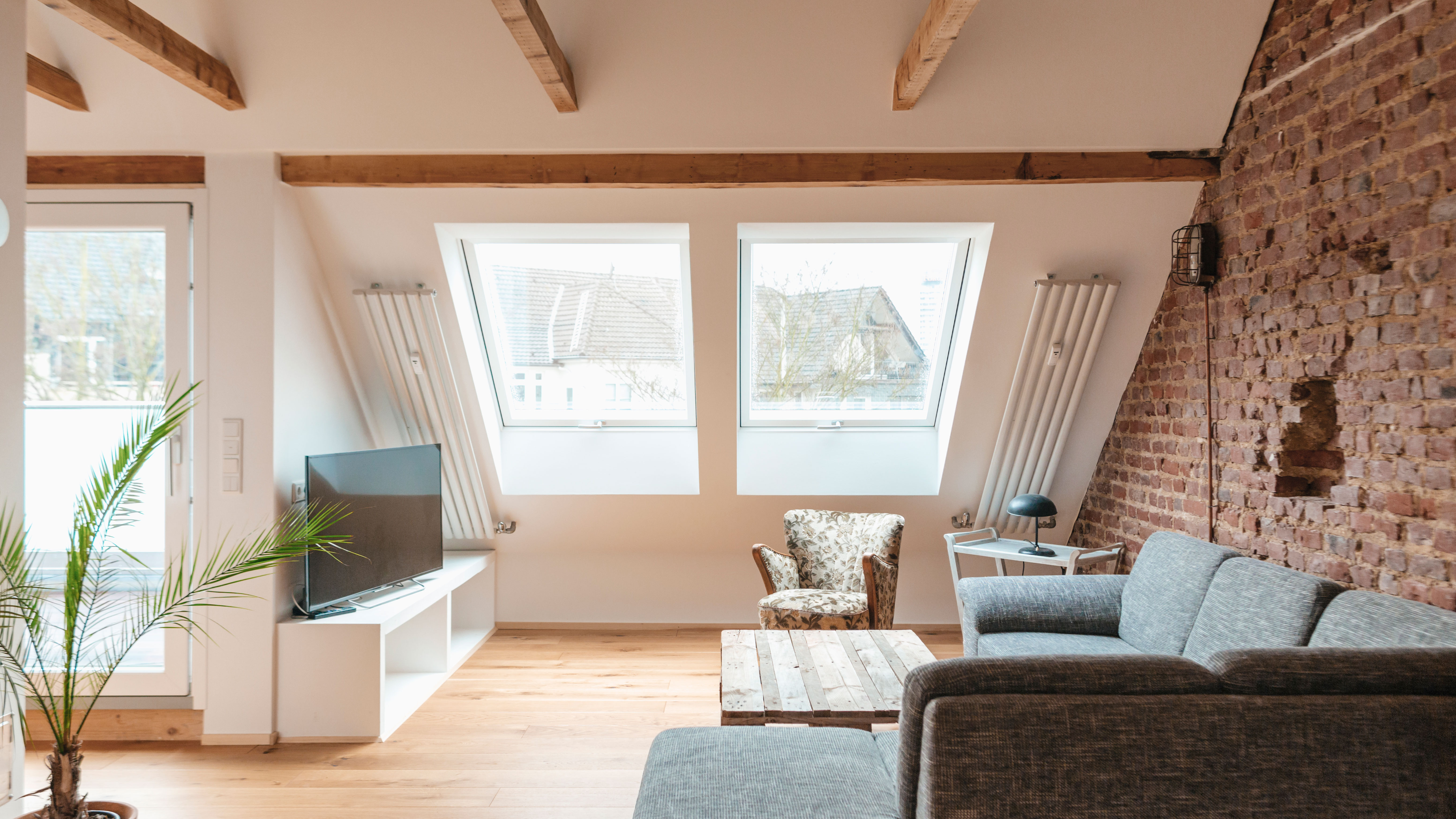 a neutral attic loft conversion with sloping windows, a sofa, chair and a TV