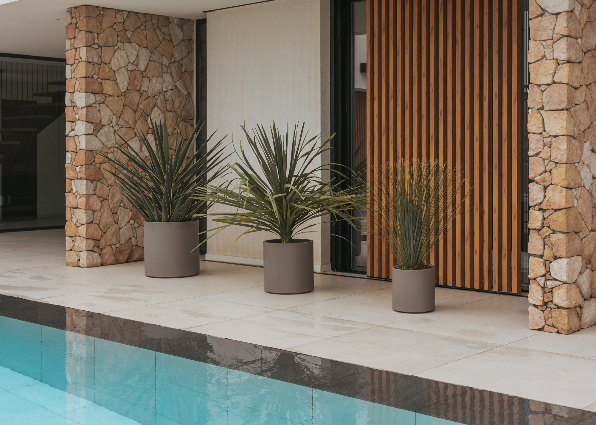An outdoor space with a set of cylindrical planters beside a pool