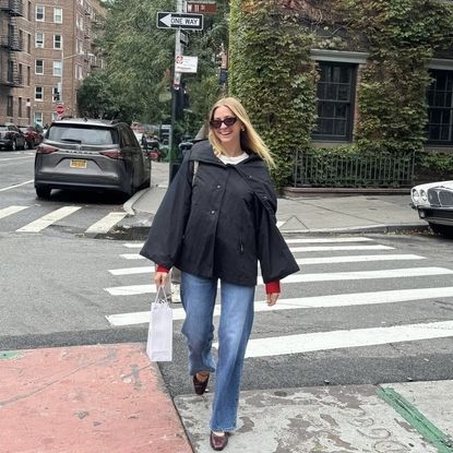 bailey burke crossing the street in NYC wearing jeans and a black rain slicker