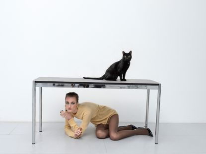 Woman in best of S/S 2023 Raf Simons under desk with black cat on it