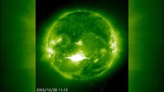 The sun viewed through a green filter with a massive flash of light erupting from its surface