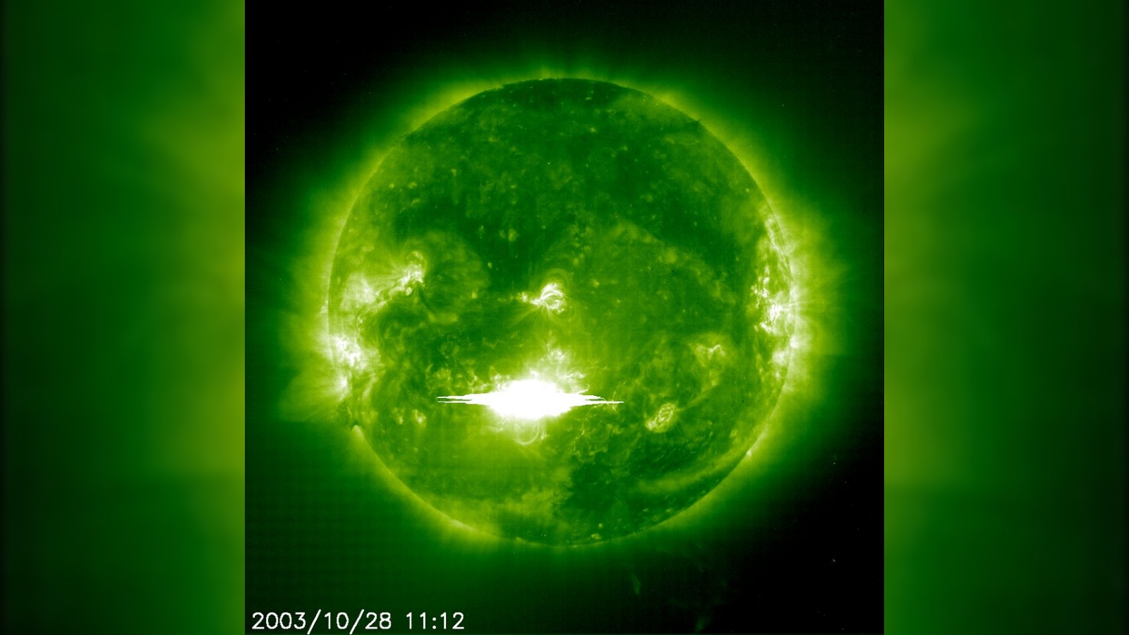 The sun viewed through a green filter with a massive flash of light erupting from its surface