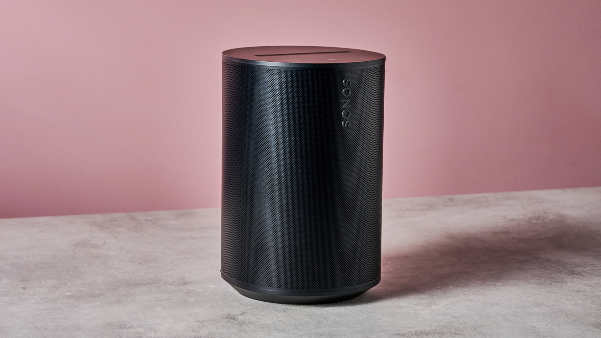 The Sonos Era 100 in front of a pink background.