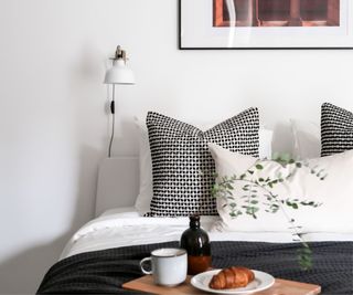 scandi bedroom with a black throw blanket, textured throw pillows and simple white walls with a food serving tray