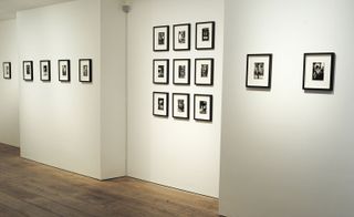 Black and white photos in black frames hanging on walls of a gallery with white walls and wooden flooring