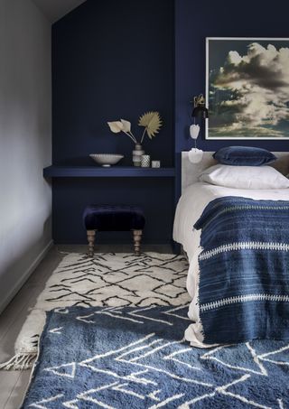 Bedroom with bed and nightstand and stool, blue wall behind bed and gray wall and rugs on wood floor