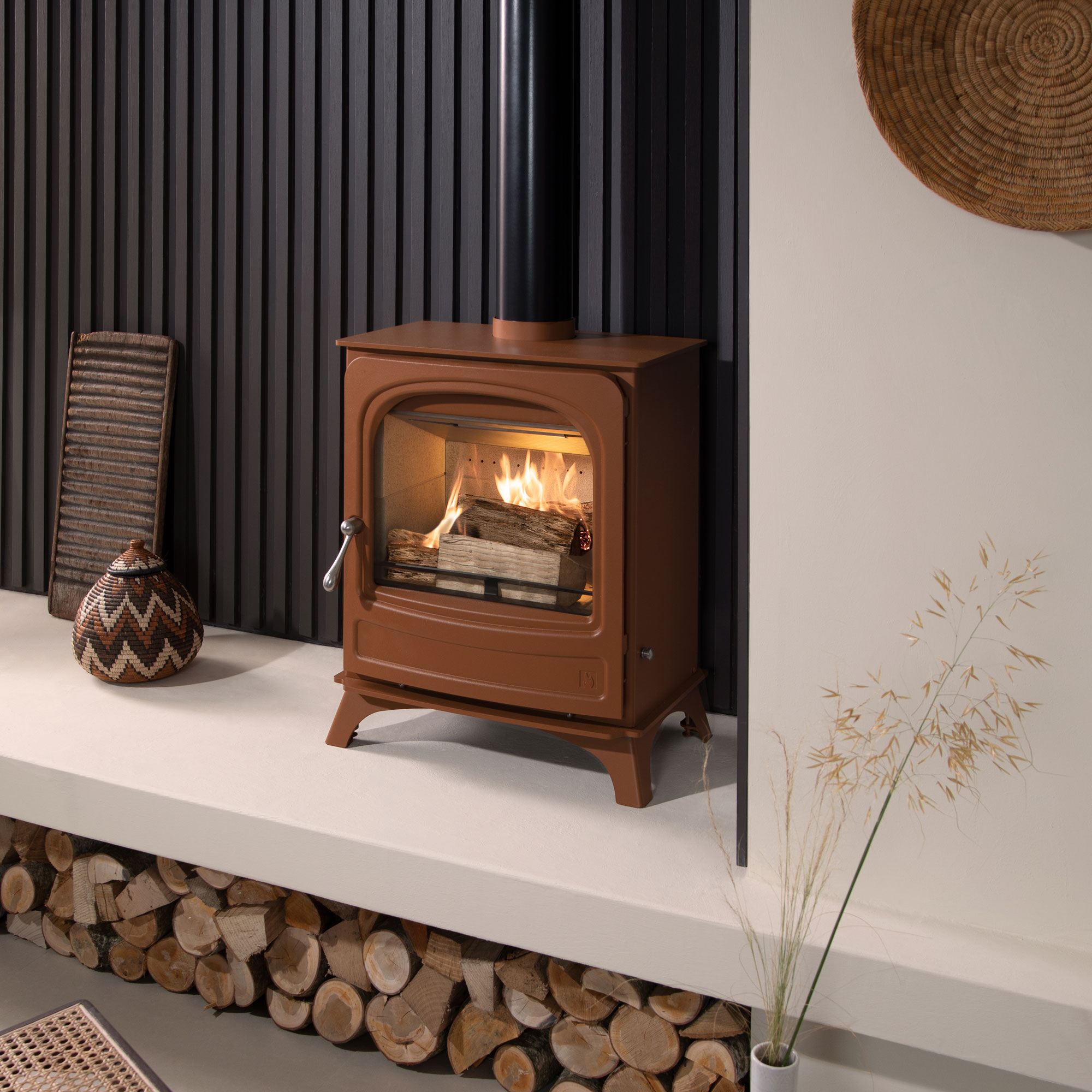 Brown freestanding log burning stove sitting on modern raised hearth with log storage beneath