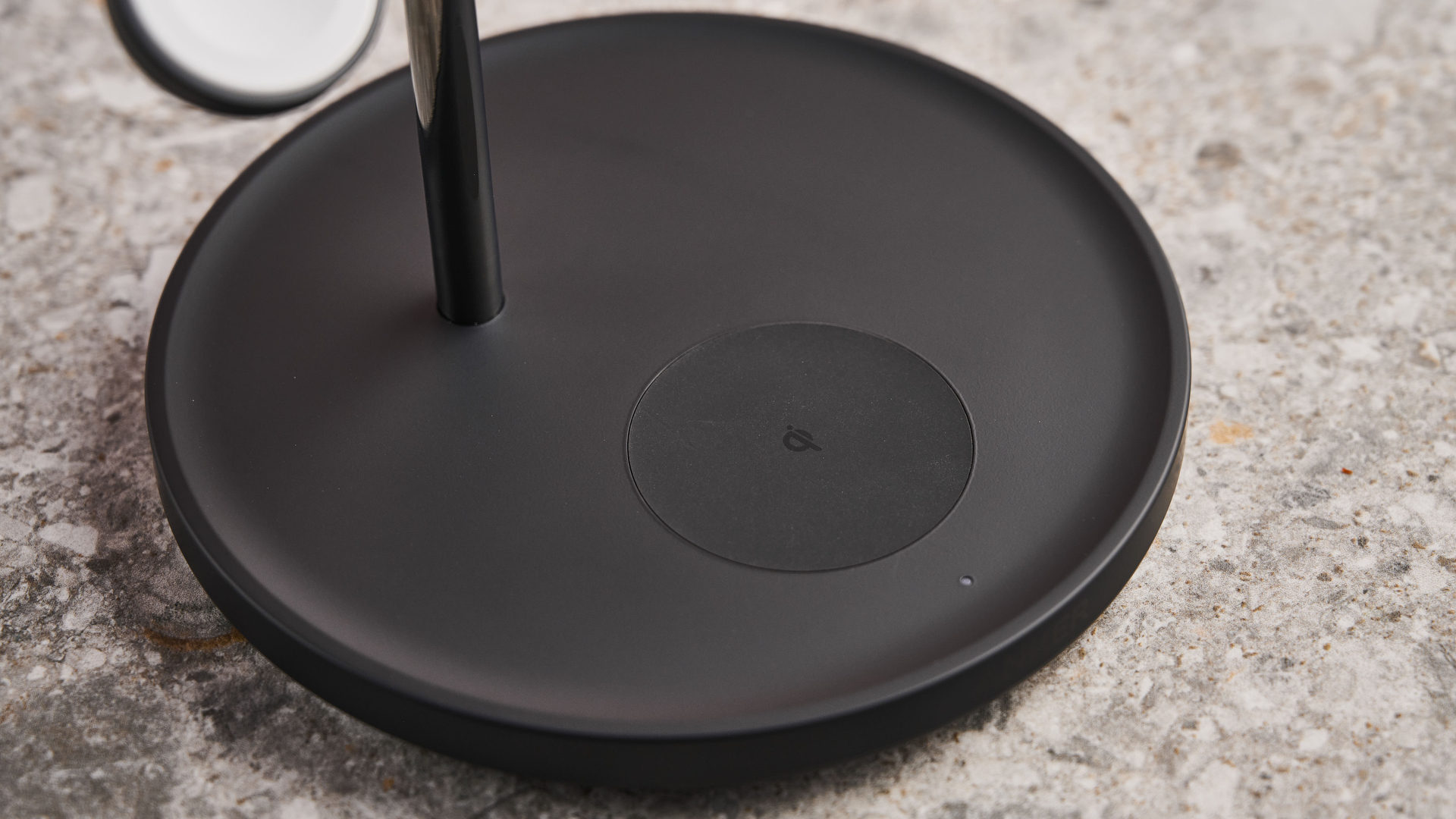 The image shows the black bass of the charging station, showing the silicon-textured circular AirPods charging pad and the indicator light.