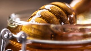 Honey sitting in glass container with wooden spoon