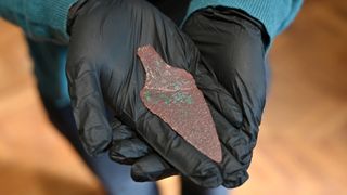 A researcher in black gloves showcases a copper dagger more than 4,000 years old.
