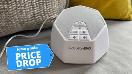 The LectroFan EVO White Noise Machine perched on a grey couch. In the lower left-hand foreground, there's a PRICE DROP deal badge. 