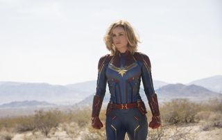 Brie Larson as captain marvel, standing in her costume in a field, in captain marvel