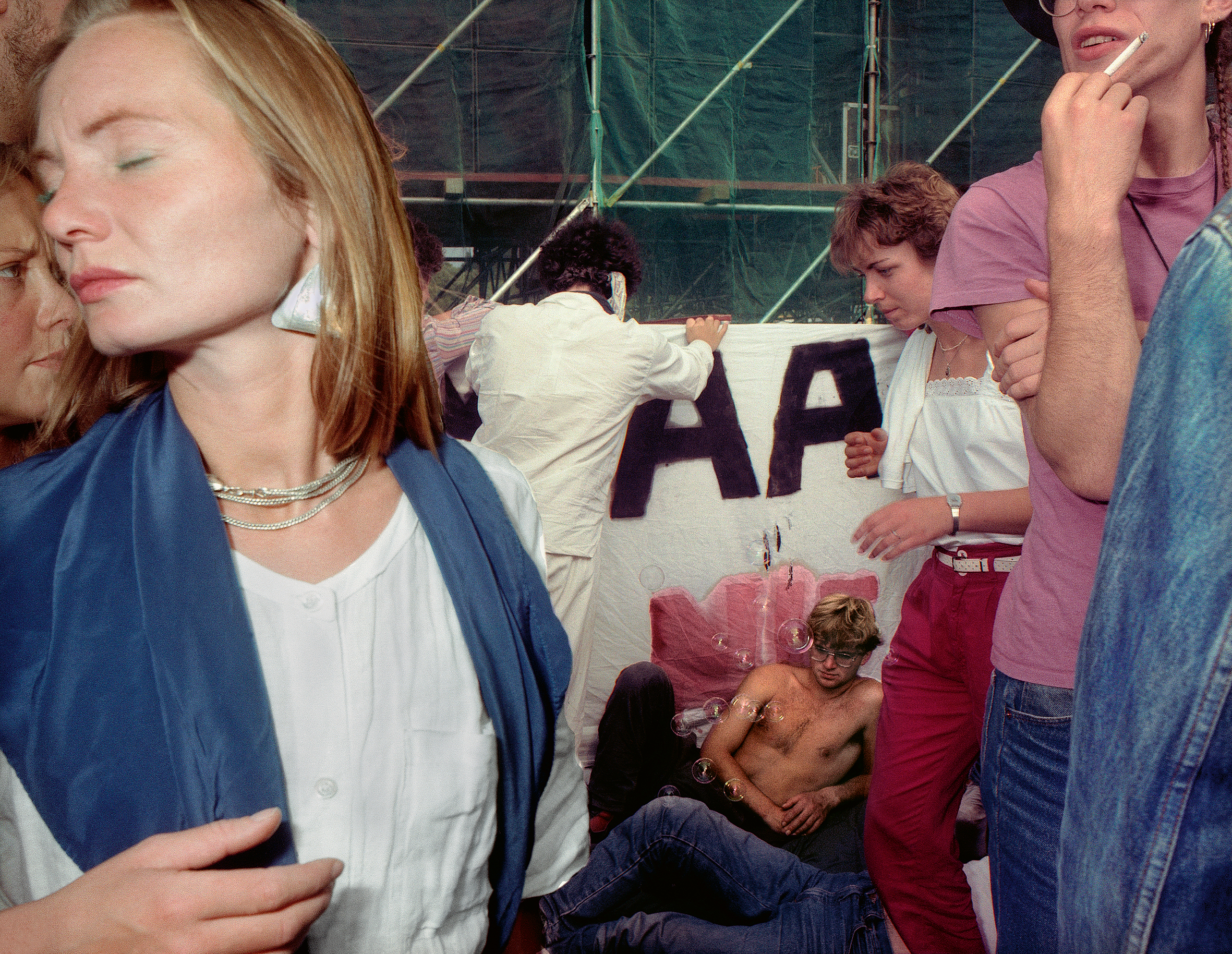 At the 1986 Wackersdorf anti-nuclear protest, a woman with her eyes closed and a scarf draped over her shoulders stands in front of a hand-painted banner reading "AA"