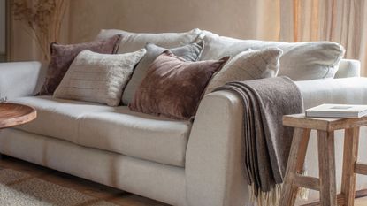 A close up of a large cream sofa with fall colored cushions. a wooden side table with a book on it 