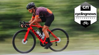 A white woman riding a red Trek road bike riding past a green background