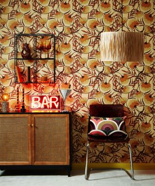 A vintage style living room with patterned orange and brown wallpaper, a console table with a neon sign, and a brown chair