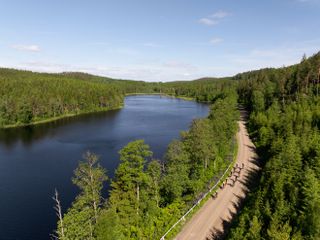 A group of gravel cyclists in Sweden ride through a forest with a large lake beside the road