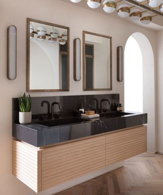 A bathroom trend in 2021 of a fluted vanity unit with black sink top and double mirrors.