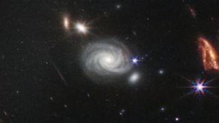A perfect spiral galaxy swirls off to the side of the central galaxy cluster.