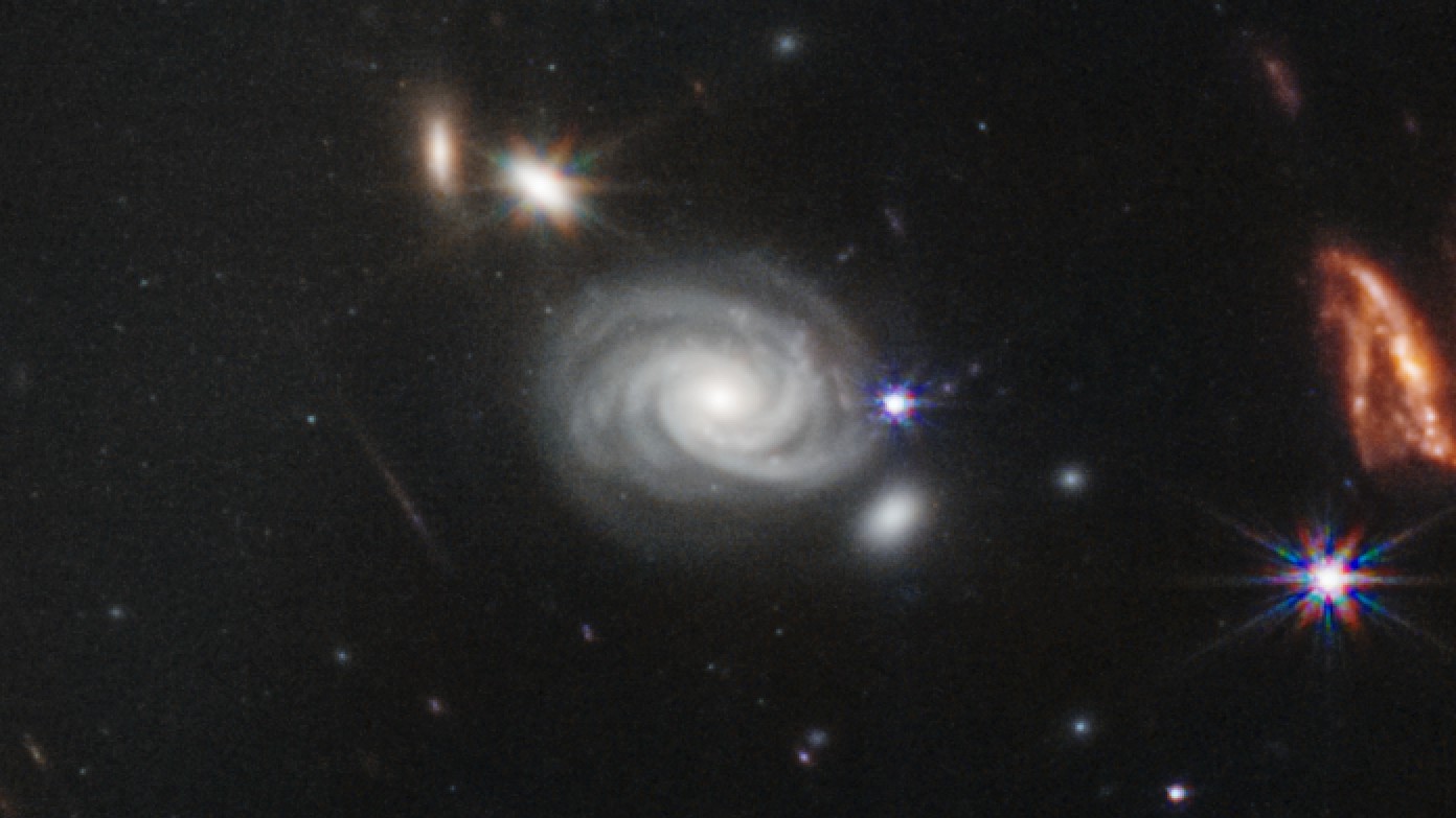 A perfect spiral galaxy swirls to the side of the central galaxy cluster.