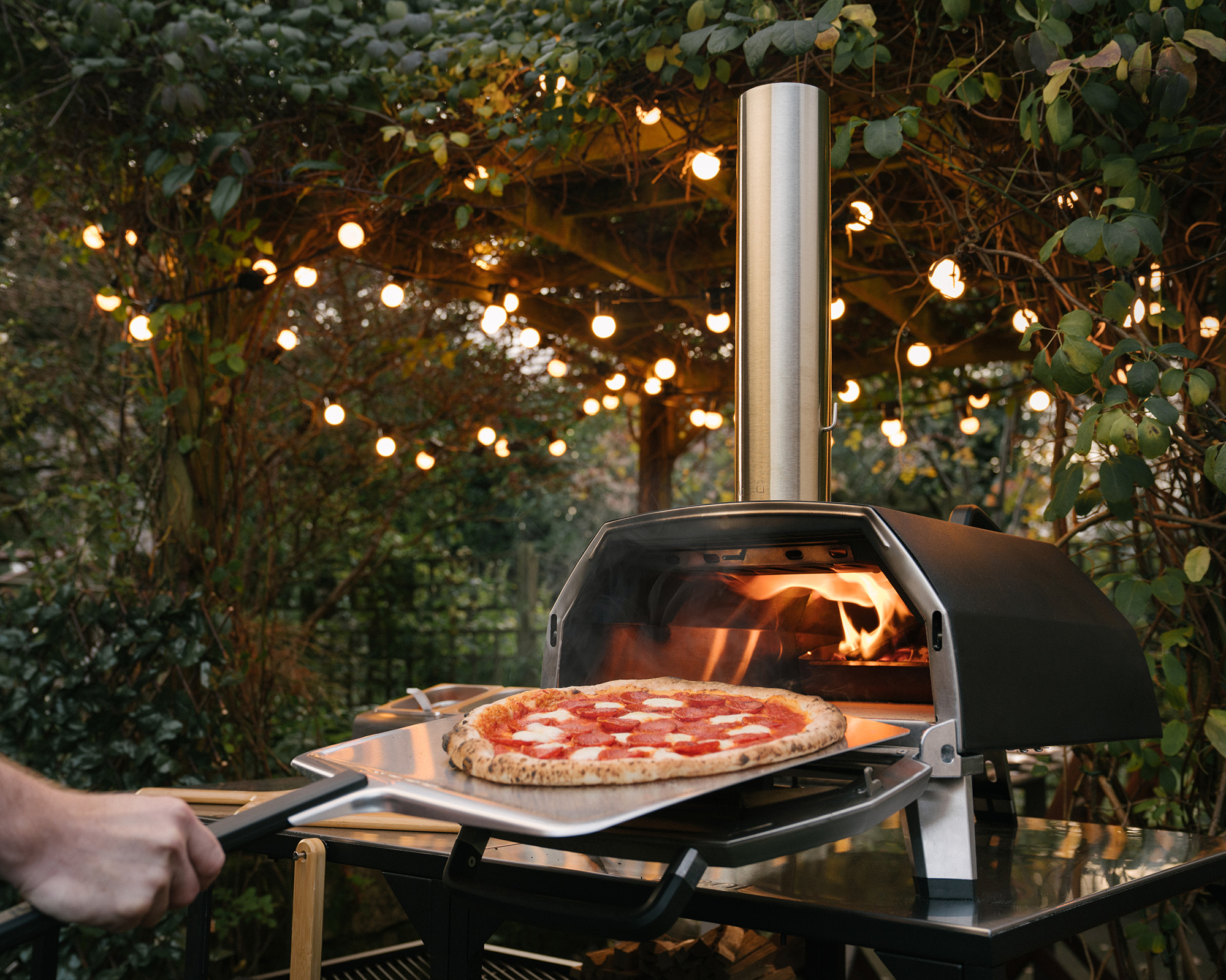 An Ooni pizza oven with a delicious pizza on a paddle